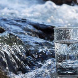 Glass of water with flowing stream in background. Sourced from istock, copyright restrictions apply.