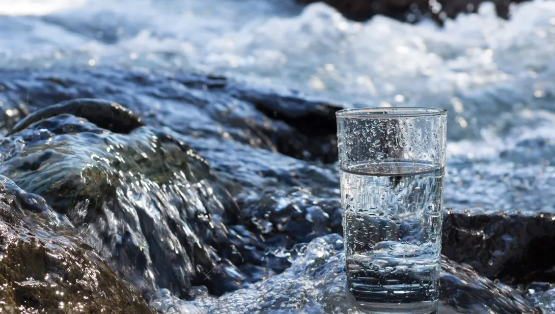 Glass of water with flowing stream in background. Sourced from istock, copyright restrictions apply.